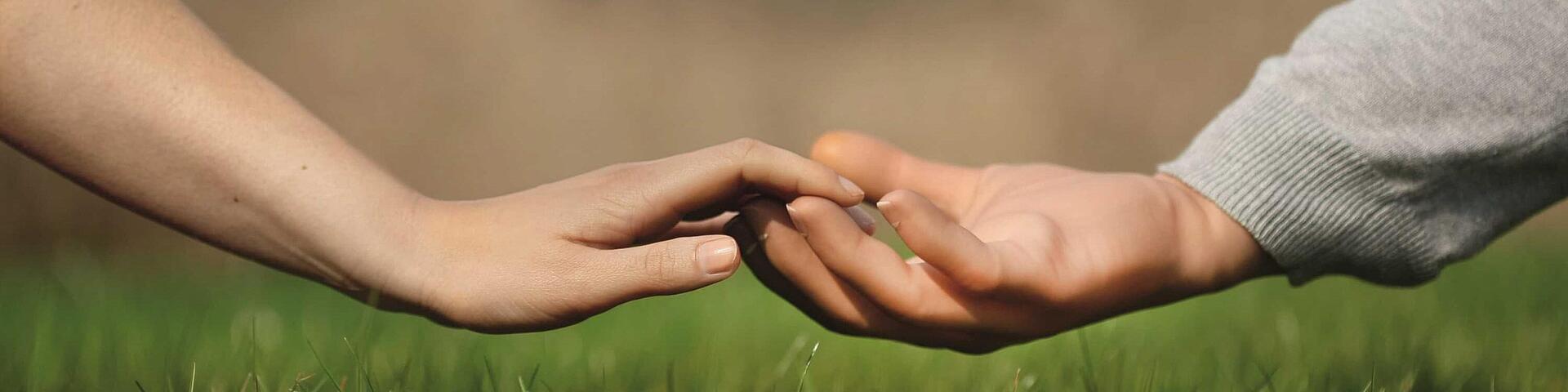 Hand in Hand, © Ottobock natürliche Hand berührt Prothesenhand über einer Wiese, © Ottobock